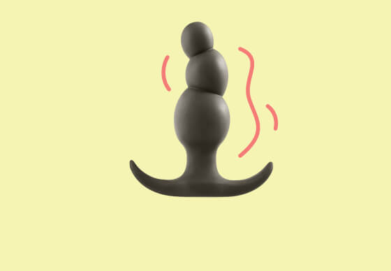 Black silicone beaded anal plug on a pale yellow background with motion marks